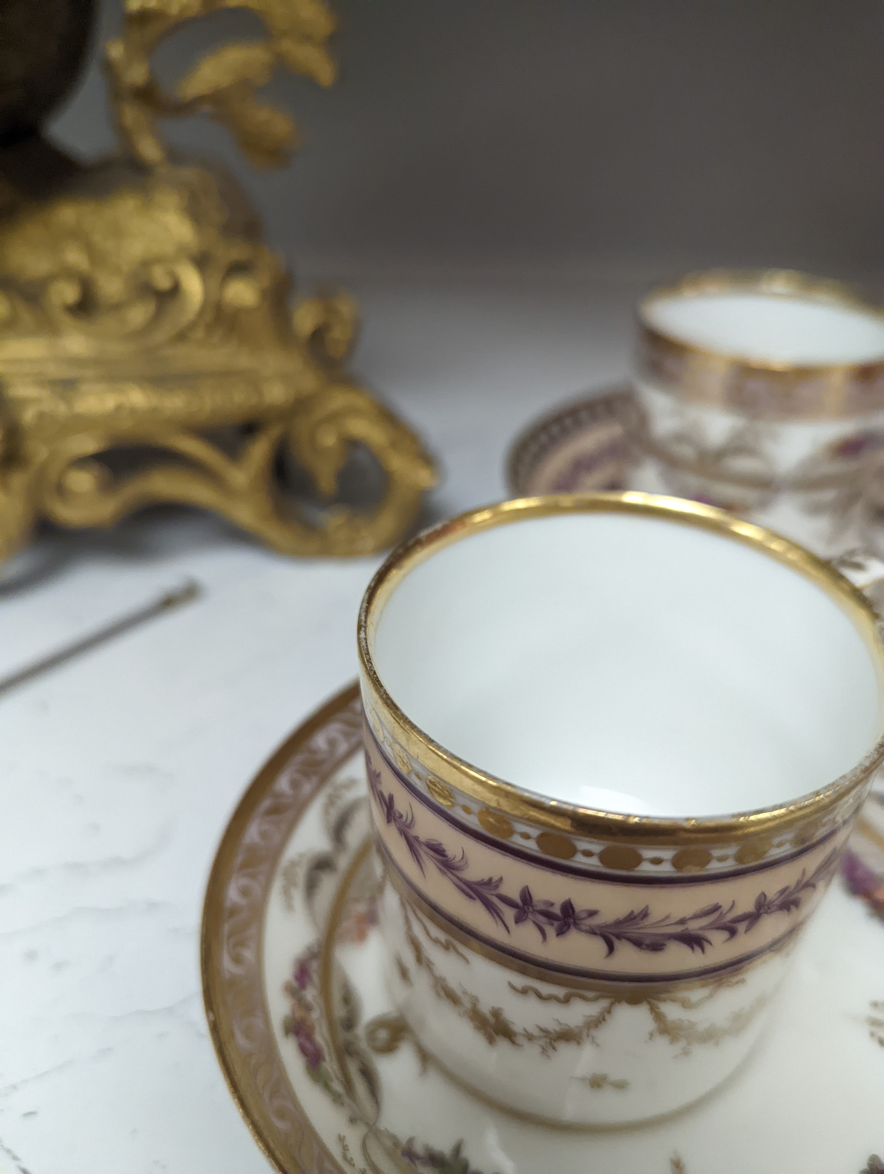 A Duc d'Angouleme coffee can and saucer painted with a puce chain of leaves on a salmon coloured ground and another painted with a flower chain, black feather and a gilt line, latter with stencilled red mark 'Manuf de M